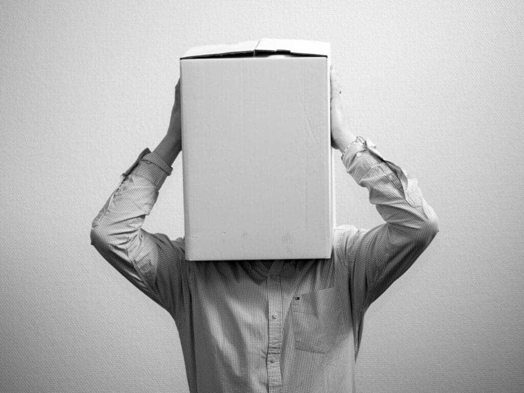 Un uomo che si copre la testa con una scatola. Una rappresentazione del desiderio di fuga dal dolore o da situazioni spiacevoli